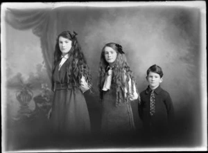 Studio portrait of two unidentified girls, with long hair worn in ringlets, wearing ribbons, and a boy wearing a spotted tie, probably Christchurch district