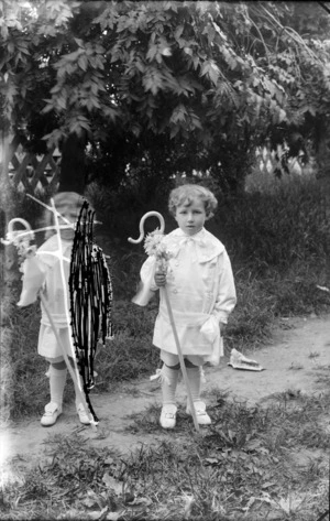 Unidentified small boy, dressed as a Shepherd, with a crook decorated with flowers, outdoors in a garden, probably Christchurch district