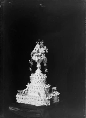 Studio portrait of a three tiered wedding cake with butterflies, swans, decorative shell icing and a vase with flowers on top, Christchurch
