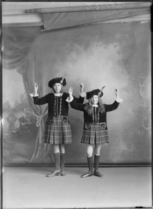 Studio portrait of two unidentified young girls in full highland dancing costumes, with kilts, doublet jackets and lace shirts, and hats with clan badges and feathers, Christchurch
