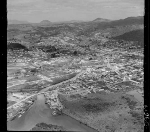 Whangarei, Northland, [Raumanga Stream?] with lumber yards in foreground and railway yards beyond, residential housing surrounding with farmland and bush covered hills