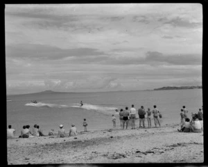 Arkles Bay, Whangaparaoa Peninsula, shows people on the beach, including a man water skiing