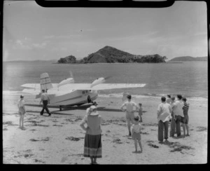 Tourist Air Travel, Grumman Widgeon aircraft ZK-BGQ at Paihia beach, Northland, includes people watching as it departs and Motumaire Island in the background
