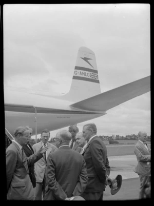 Mr Cunningham left and Mr T Shand Minister for Civil Aviation on right talking with unidentified men with TEAL Comet G-ANLO aircraft behind, Whenuapai, Auckland