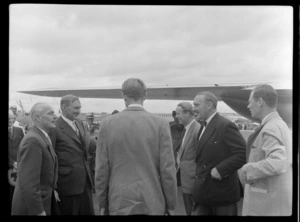 L to R, Mr J Kerr NZDH, Mr T Shand Minister for Aviation, Mr Cummingham and Mr Frank Lloyd, standing on runway with TEAL Comet aircraft and unidentified men behind, Whenuapai, Auckland