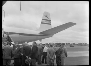 Mr Cunningham left and Mr T Shand Minister for Civil Aviation on right talking with unidentified men waiting for flight, with TEAL Comet G-ANLO aircraft behind, Whenuapai, Auckland