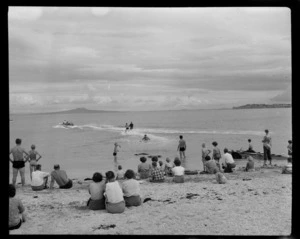 Arkles Bay, Whangaparaoa Peninsula, shows people at the beach, including two men water skiing