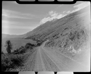 A shingle road alongside Lake Wakatipu north of Kingston Township, with steep tussock covered mountain slopes, Central Otago Region