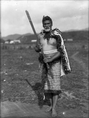 Unidentified Maori man wearing cloaks, with a taiaha