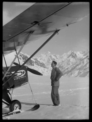 Unidentified man looks at a Mount Cook Air Services Ltd, Auster aircraft, Mount Cook Airfield, Mount Cook National Park, Canterbury Region, during the preparation for the Antarctic Expedition