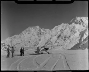 A Mount Cook Air Services Auster ZK-BLZ Ski Plane on the Tasman Glacier with unidentified people [Harry Wigley?], with Mount Cook beyond, Mount Cook National Park, Canterbury Region