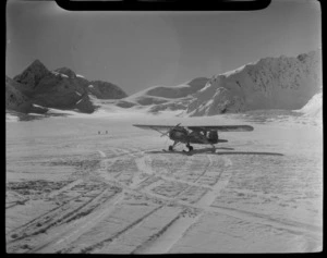 Mount Cook Air Services Auster ZK-BLZ Ski Plane and two unidentified people at the head of the Tasman Glacier with snow covered mountains beyond, Mount Cook National Park, Canterbury Region