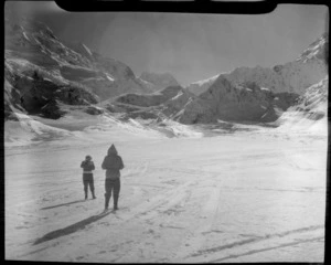 Mount Cook Air Services and two unidentified people standing at the head of the Tasman Glacier with snow covered mountains beyond, Mount Cook National Park, Canterbury Region