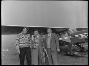 Sir Edmund Hillary with two unidentified men in front of a Mount Cook Air Services Ltd aircraft, Mount Cook Airfield, Mount Cook National Park, Canterbury Region, during the preparation for the Antarctic Expedition
