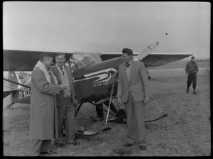 Three unidentified men standing in front of a Mount Cook Air Services Ltd aircraft, Mount Cook Airfield, Mount Cook National Park, Canterbury Region, during the preparation for the Antarctic Expedition