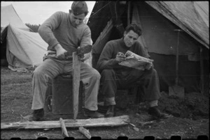 Private O J Spinetto cuts firewood while Corporal H Kingston reads at the NZ LOB Camp, Italy, World War II - Photograph taken by George Bull