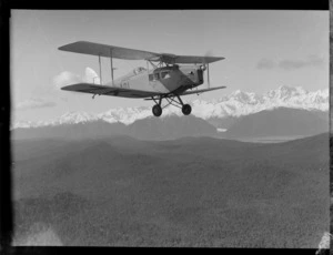 Air Travel New Zealand Ltd de Havilland DH 83 Fox Moth aeroplane, in flight, with snow-covered mountain range in distance