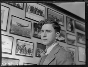 Portrait of D C Morris, Musick Point, Auckland region, in front of wall of framed photographs