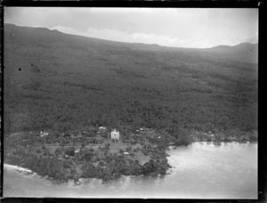 Aerial view of a coastal village with a three story stone [church?] and fale tele huts, with palm trees beyond, Apia, Western Samoa