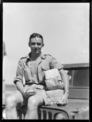 Portrait of an unidentified 'Air Moments Sergeant' sitting on the bonnet of a jeep with the latest mail delivery from home, Tonga