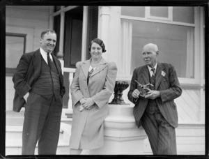 Portrait of Mr & Mrs C Rootes with Mr A Whitelaw holding a model plane, outside a wooden building, Rongotai, Wellington