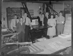 Portrait of Leader Press Group unidentified personnel in their workshop standing beside a printing press, location unknown