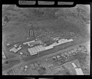 View of the NZ Forest Products' Pinex Factory with buildings and stacked wood, with railway line and roads, Penrose, Auckland