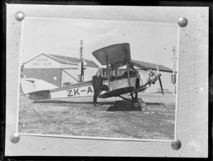 Copy photograph of a portrait of [H T Parry?] and his Robinson Redwing Tiger Moth bi-plane ZK-ADD in front of the Hokitika Aero Club hangars, Hokitika