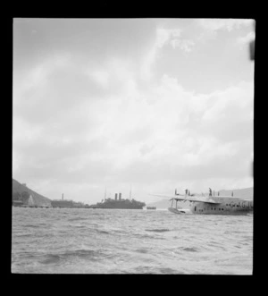 The arrival of the BOAC Hobart G-AGJL, a Short Hythe flying boat, at Evans Bay wharves with a large steamship beyond, Wellington Harbour
