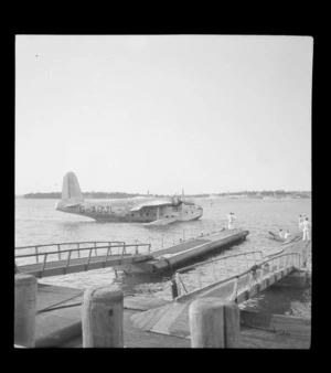 The arrival of the BOAC Hobart G-AGJL, a Short Hythe flying boat, at Mechanic's Bay wharves with unidentified personnel in foreground, Auckland Harbour