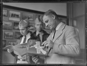 Portrait of John C Boyle, of Pan American Airways, reading Leo White's 'Wingspread' book in Whites Aviation Offices, with two unidentified PAA [pilots?] behind, Whites Aviation Offices, Auckland