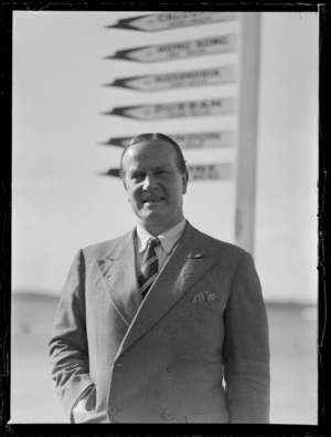 Portrait of Air Commodore H G Brackley of BOAC in front of sign posts, Mechanics Bay, Auckland Harbour