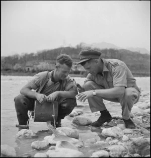 Lieutenant W Moffett and D Brown inspecting larvae at the edge of the Volturno River, Italy, World War II - Photograph taken by M D Elias