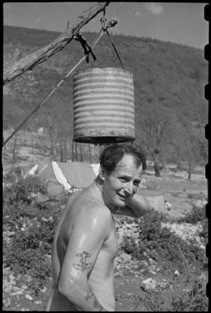 J R A Chote makes use of a crudely constructed shower at 6 NZ Field Ambulance in Italy, World War II - Photograph taken by George Bull