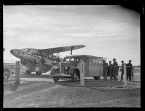 View of a De Havilland DH86 Union Airway's (UA) ZKAHW bi- plane 'Korimako', with unidentified passengers boarding a UA bus, Mangere Airfield, Auckland