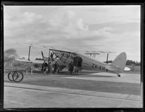 View of a De Havilland DH86 Union Airway's ZKAHW bi-plane 'Korimako' with unidentified passengers disembarking, Mangere Airfield, Auckland