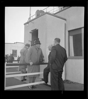 TEA group members Sir Leonard Isitt and F Maurice Clarke with three other unidentified TEA members in front of a building, Mangere Airfield, Auckland