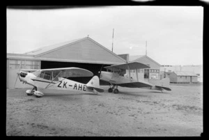 View of Auckland Aero Clubs' ZK-AHE Taylor Cub and Tiger Moth in front of a hangar, Mangere Airfield, Auckland