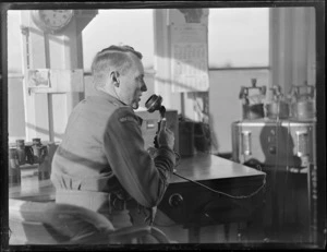 Portrait of an unidentified man operating a radio transmitter in the Mangere Control Tower, Auckland