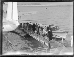 Tasman Empire Airways Ltd seaplane docks at Mechanics Bay, Auckland, showing passengers disembarking from the aircraft and walking on the gangway to shore