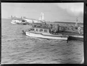 Mechanics Bay, Auckland, showing three unidentified men working on the boats at the dock, with the aircraft Tainui in the background