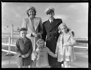 Portrait of Captain D Phillips of Tasman Empire Airways (TEA), in uniform with his family, [Auckland City waterfront?]