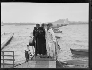 Arrival of TEAL Short Tasman Flying Boat ZK-AMA 'Australia' with unidentified crew helping an older woman passenger up the dock ramp in foreground, Mechanic's Bay, Auckland City