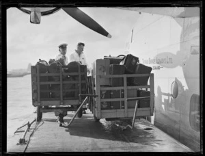 View of two unidentified TEAL luggage handlers loading TEAL Short Empire Flying Boat ZK-AMA 'Awarua' at Mechanic's Bay wharf, Auckland Harbour