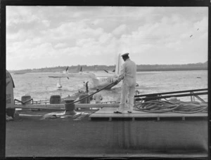View of an unidentified TEAL employee with rope mooring TEAL Short Empire Flying Boat ZK-AMA 'Awarua' to Mechanic's Bay wharf, Auckland Harbour