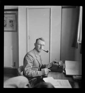 Portrait of T [Ewart?] of Whites Aviation Office sitting at his typewriter with a pipe, Auckland City