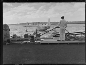 View of an unidentified TEAL employee with rope mooring TEAL Short Empire Flying Boat ZK-AMA 'Aotearoa' to Mechanic's Bay wharf, Auckland Harbour