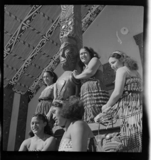 Group of Māori women, including guide Bubbles Mihinui, gathered around a carved and decorated meeting wharenui building