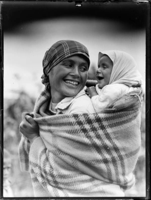 Unidentified Maori mother with a baby on her back wrapped in a blanket, both are wearing head scarves