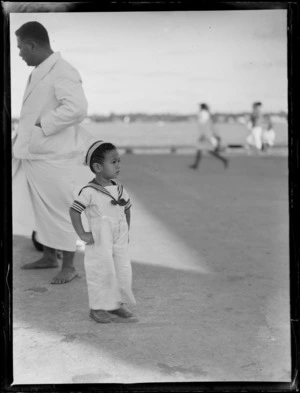 A close-up portrait of local Tongan child in a sailors outfit and unidentified man behind, Tonga